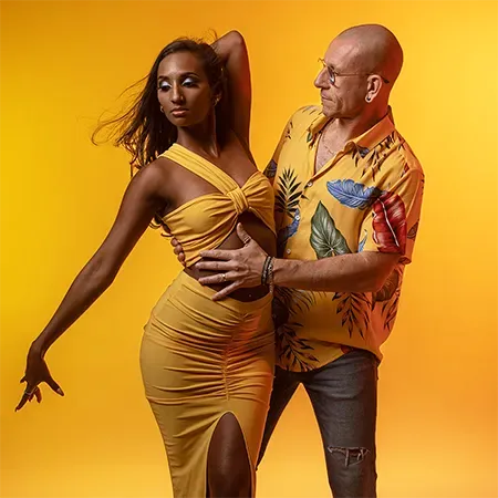 Saint-Just et Emma en position de danse sur fond jaune : Emma cambrée, un bras levé, Saint-Just derrière elle